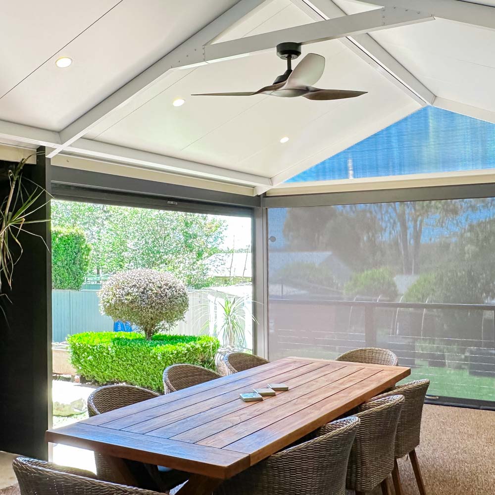 Outdoor dining area under an insulated patio awning with down lights and a ceiling fan by Sydney Patios